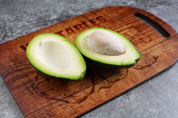 two halves of an avocado. avocado seed. wooden cutting board. artificial stone board. diet food.