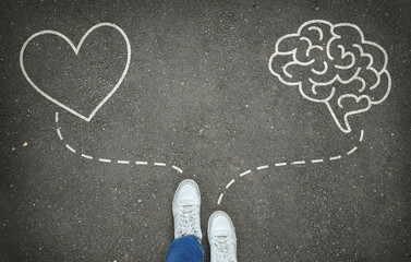 Heart or brain. Legs in white sneakers in front of white heart and brain symbols on the gray...
