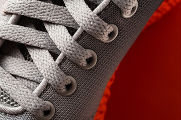 Lacing of gray textile sneakers with orange sole close-up. New sport shoe laced up macro. Elastic laces of modern mesh fabric trainers for fitness, sport exercises and active lifestyle.