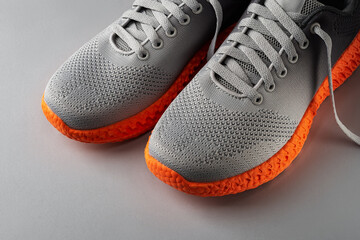 Pair of stylish gray textile sneakers with grooved orange sole over grey background. Laced up modern mesh fabric trainers for active lifestyle, running and sports exercises. Fashion sport shoes.