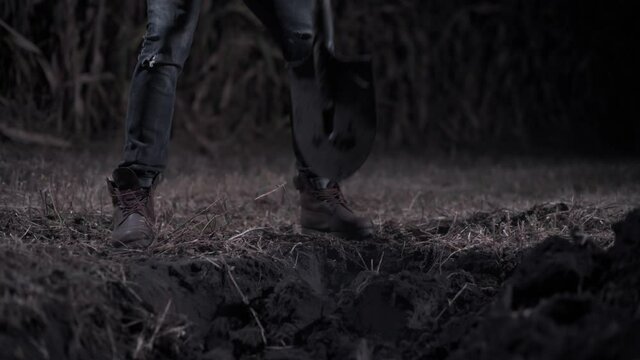 Killer digs grave at night. Young scary man digs hole in field. Medium shot.