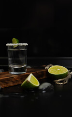 One stack of tequila with fresh lime slices and salt on stylish wooden board on black background