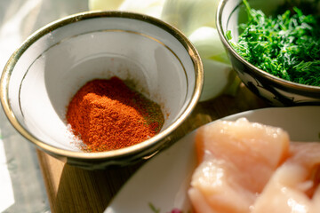 Dry grated paprika and greens next to raw chicken. Spices, herbs and raw meat