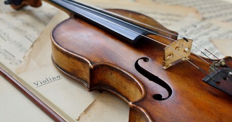 An old antique violin on a table with yellowed sheet music close-up.
