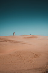 Fototapeta na wymiar Exploring the famous ancient Rubjerg knude fyr place in the endless sand dunes. Desert like sand dunes with the landmark lighthouse on a bright summer vacation day. North Jutland, Denmark, Europe