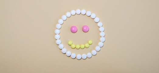 smiley face laid from yellow white pink pills on beige background. Happy life