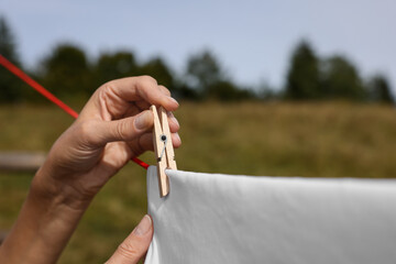 Woman hanging clean laundry with clothespin on washing line outdoors, closeup