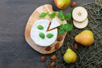 white brie cheese on a wooden board on a dark slate, concrete or stone background with basil, almonds and pears. top view. the concept of proper nutrition.