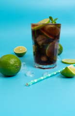 summer cooling cocktail with rum, ice and ripe lime sliced into wedges on a blue background