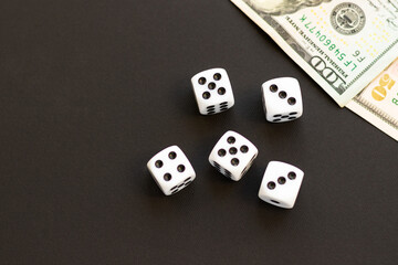 Dice and blurred 100, 50 US dollar on black. Fortune, gaming addiction. Playing cube with numbers. Items for board games. Flat lay, top view, copy space.
