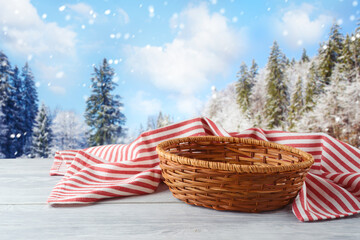 Empty basket with tablecloth on wooden table over winter landscape background.  Christmas and New...