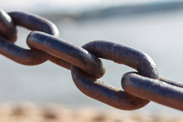 Heavy forged chain on the fence of the Neva embankment. The links of an old chain, illuminated by the sun, close-up.
