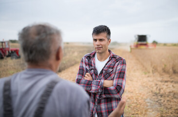 Two male farmers standing in harvested soy field talking.