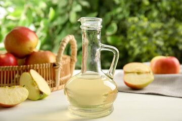 Natural apple vinegar and fresh fruits on white table against blurred background