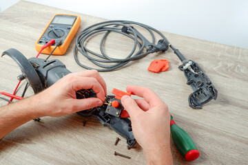 Power tool repair. A man repairs an angle grinder. Screwdriver, multimeter. Details of electrical appliance