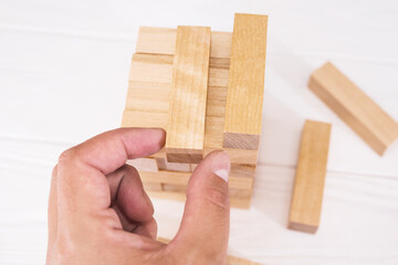 Tower made of wooden blocks and human hands take one block