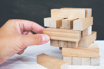 Tower made of wooden blocks and human hands take one block