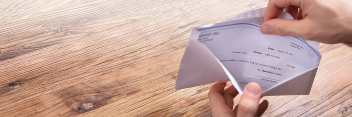 Person's Hand Removing Paycheck From The Envelope