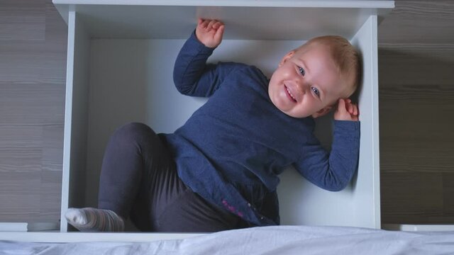 Caucasian Female Revealing Happy Adorable Cute Caucasian Baby Toddler Girl Hiding in Bed Drawer for Pillows and Sheets