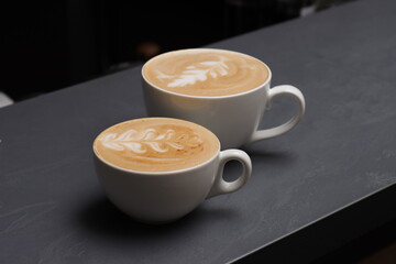 Two white cups with latte coffee on a gray background
