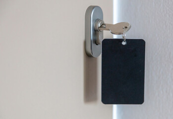 Steel key ring with blank label for text or number and hotel room door key in the keyhole, closeup