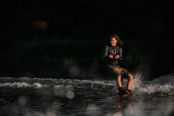 wet man in wetsuit energetically balancing on water surface on wakeboard