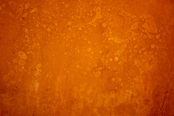 Abstract bright orange background made of water drops with oil on the glass surface. View from above.