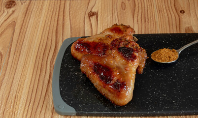 Two chicken wings baked with honey and mustard lie on a dark cutting board. On the right is a...
