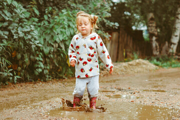 a child runs through puddles in rubber boots