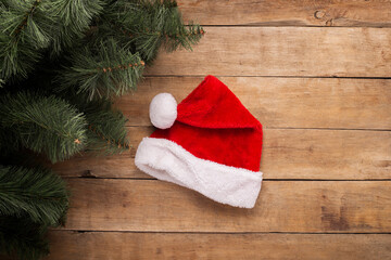 Obraz na płótnie Canvas Christmas background. Santa Claus hat and branches of a Christmas tree on a wooden background. Top view, flat lay