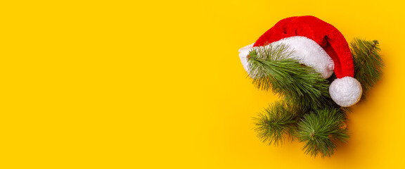 Christmas tree with a Santa Claus hat peeps out of a hole in a yellow background. Concept for New Years and Christmas Eve. Banner