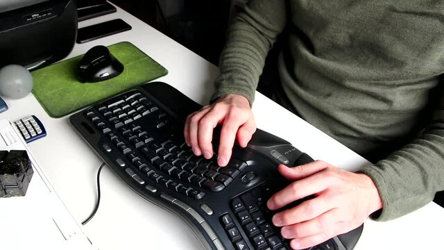 Stressed home office man using pen or fidget spinner for stress relief while working from home at ergonomic keyboard and ergonomic mouse at white desk with european man hands compense job work load