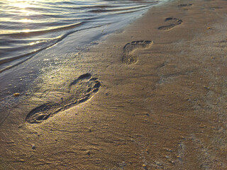 Footprints in the sand at sunset. Beautiful sandy tropical beach with sea waves. Footsteps on the shore.