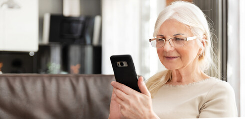 Beautiful senior woman texting at home