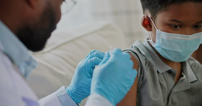 Young african american male doctor injecting flu or corona virus vaccine for a boy patient in a health clinic. Medical nurse use hypodermic needle and a syringe put shot of drug for treatment.