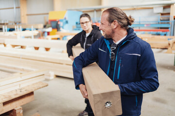 Co-workers carrying a large timber beam in a carpentry workshop