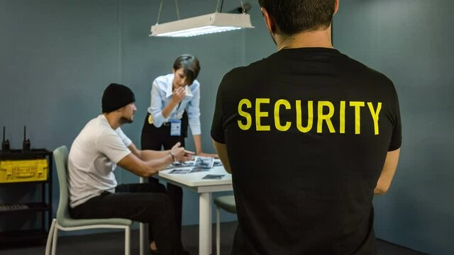 Detective interrogating a suspect in dark room under surveillance by security