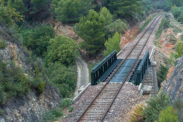 Narrow train track crossing a natural landscape on a cloudy day.