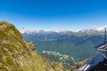 The rope bridge on the top of mountain of Rosa Khutor. Spring mountain landscape with green mountains and snow peaks.