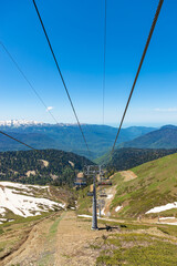 Fototapeta na wymiar SOCHI, KRASNAYA POLYANA, RUSSIA - MAY 31, 2021: Funicular panorama in the Caucasian mountains. Open cabins cable car Roza Khutor. Spring in the mountains.