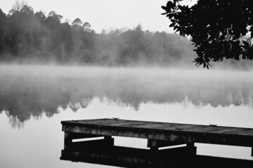Grayscale of a wooden pier on a lake on a foggy morning