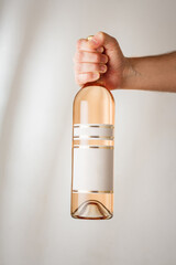Male hand holds big bottle of pink wine or rosa champagne with no brand label, mockup template. Vertical shot, white background