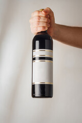 Male hand holds big bottle of red semisweet sweet or dry wine with no brand label, mockup template. Vertical shot, white background