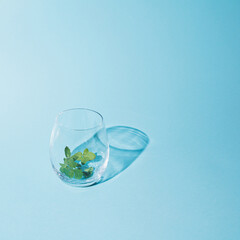 Empty clear glass with green mint leaf. Minimal concept on bright blue background. Quench your thirst with refreshing drink.