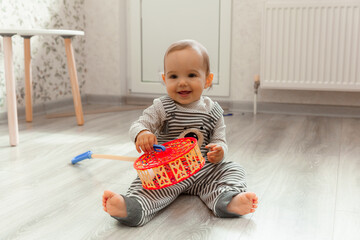 cute smiling baby 12 months old sits on the floor in his room and plays with toys.