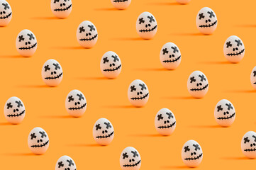 Halloween pattern made of white eggs painted as ghost characters on orange background