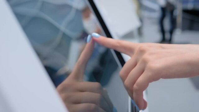 Woman hand using interactive touchscreen display of electronic multimedia terminal at modern museum or exhibition - close up. Education, innovation, futuristic and technology concept