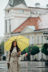 Woman wearing a yellow umbrella and walking during a heavy rain in the city