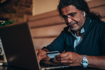 Senior hispanic cuban men using laptop and a credit card while online shopping