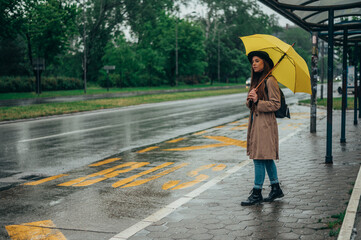 Woman holding yellow umbrella and waiting for public transportation